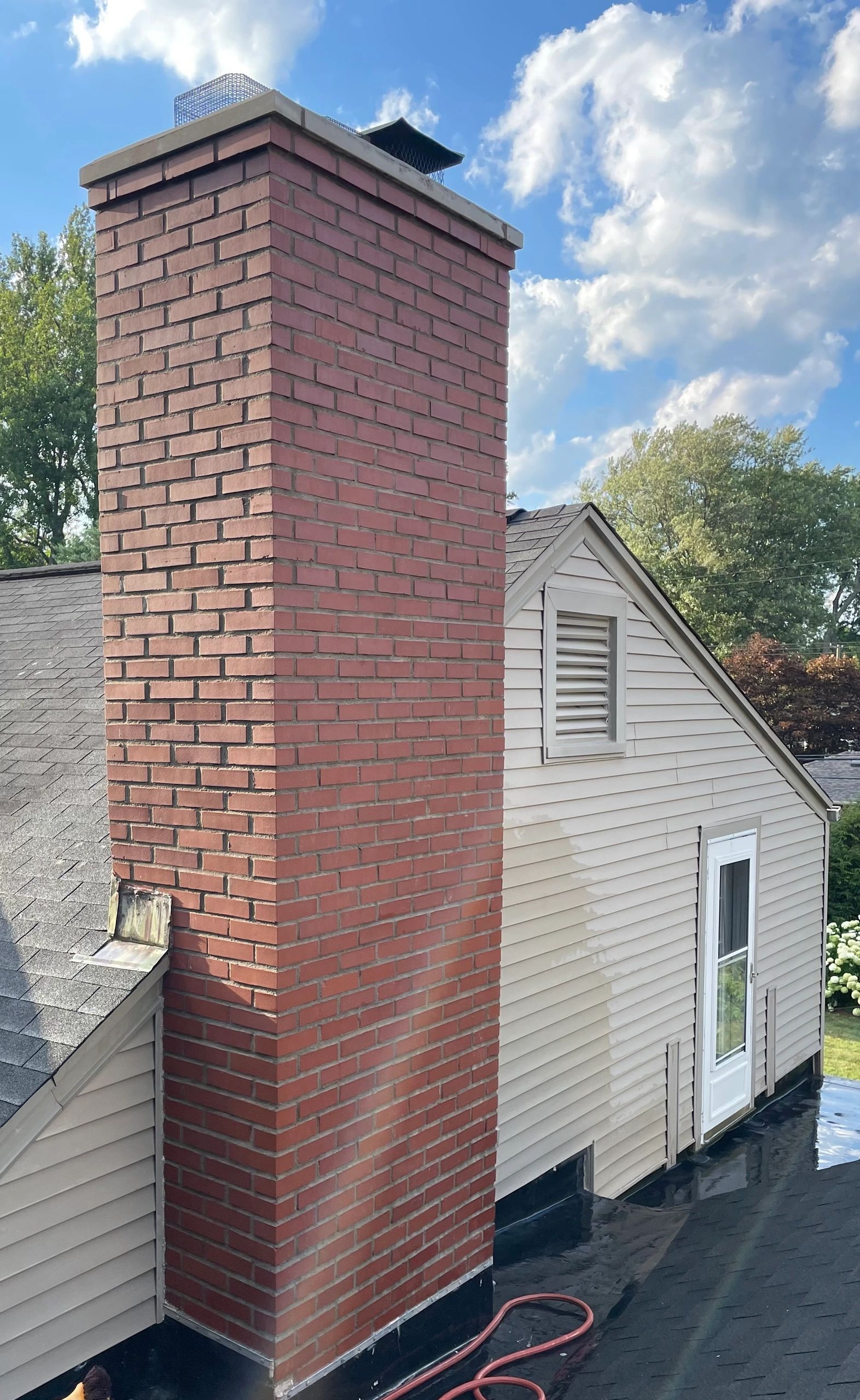 Tall red brick chimney restoration against blue sky